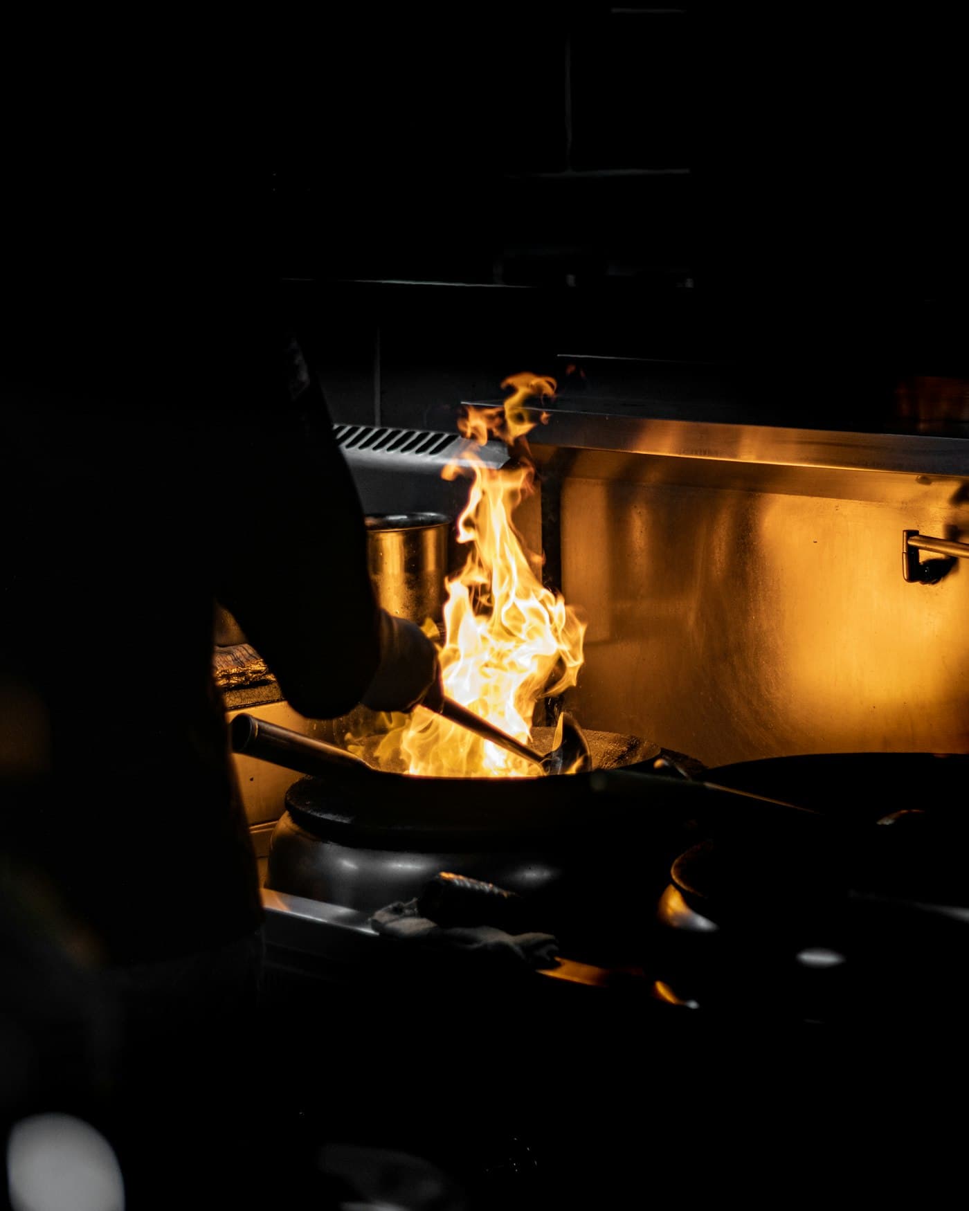Flames rising from a wok in a dark kitchen